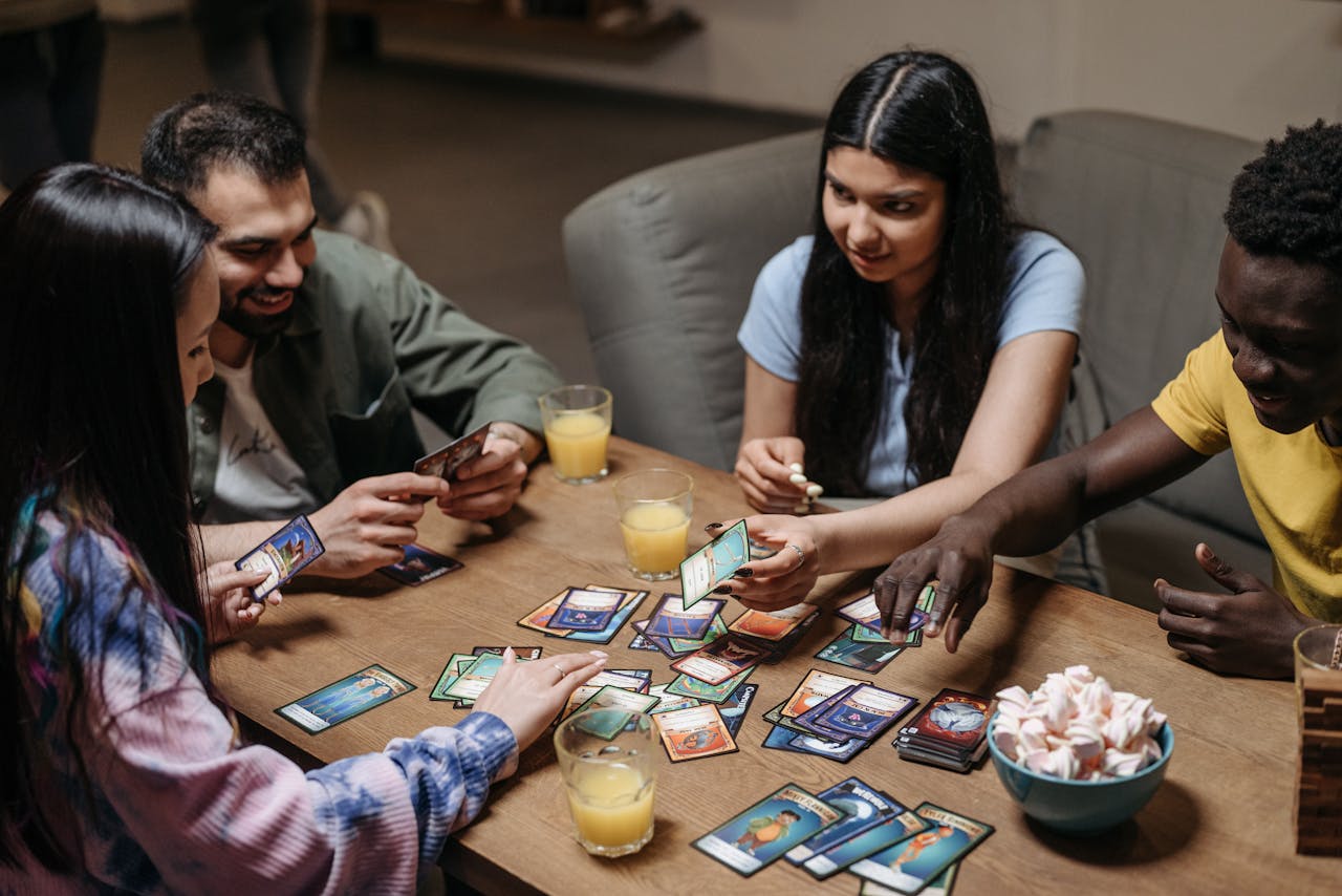 A diverse group of friends playing card games at a table with drinks, showcasing socialization and togetherness.